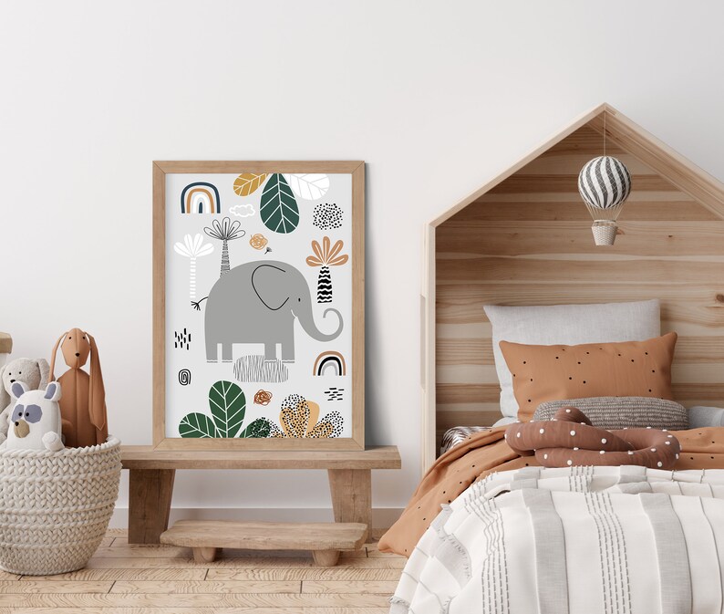 May include: A framed print with a whimsical illustration of an elephant standing on a rock surrounded by green leaves and colorful geometric shapes. The print is in a light wood frame and is hanging on a white wall.