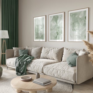 May include: A light beige sectional sofa with three pillows, a green throw blanket, and a wooden coffee table with books and a decorative bowl. The sofa is in a living room with green curtains, a floor lamp, and a vase with dried pampas grass.
