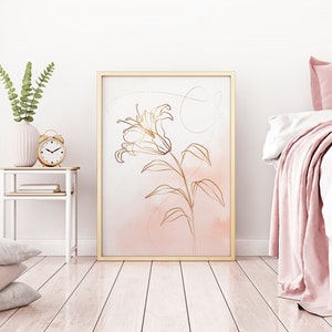 May include: A gold line drawing of a lily flower on a pink watercolor background. The drawing is framed in a gold frame and hanging on a white wall.