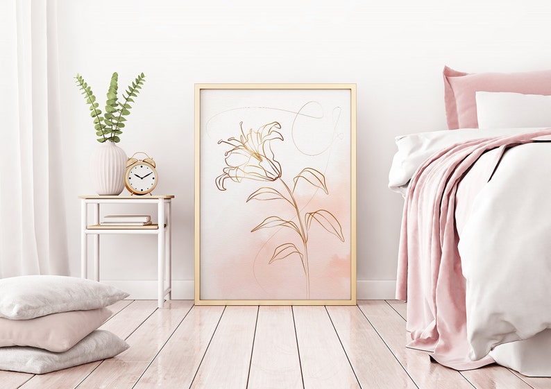 May include: A gold line drawing of a lily flower on a pink watercolor background. The drawing is framed in a gold frame and hanging on a white wall.