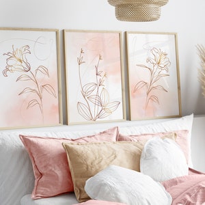 May include: Three framed prints with a minimalist line drawing of flowers in gold on a pink watercolor background.