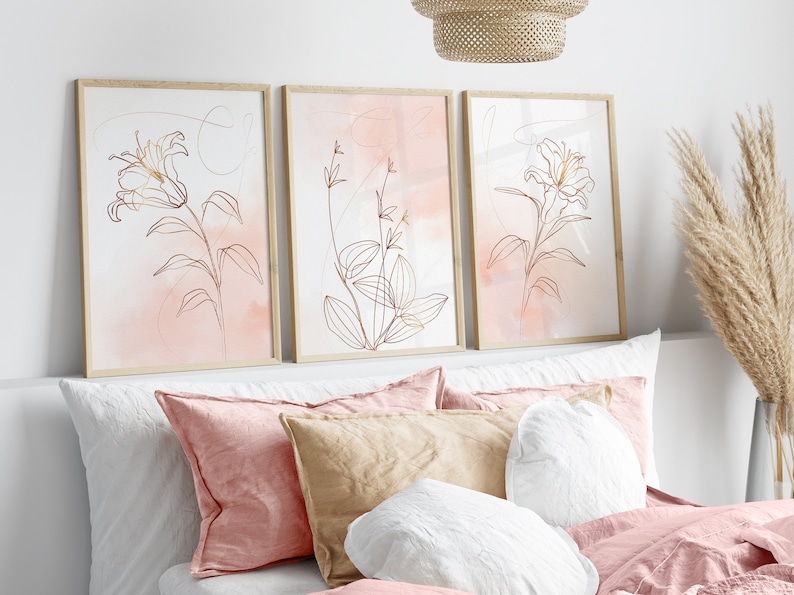 May include: Three framed prints with a minimalist line drawing of flowers in gold on a pink watercolor background.