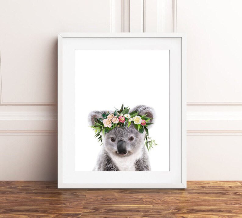 May include: A cute koala wearing a flower crown with pink, white, and green flowers. The koala is looking directly at the camera.