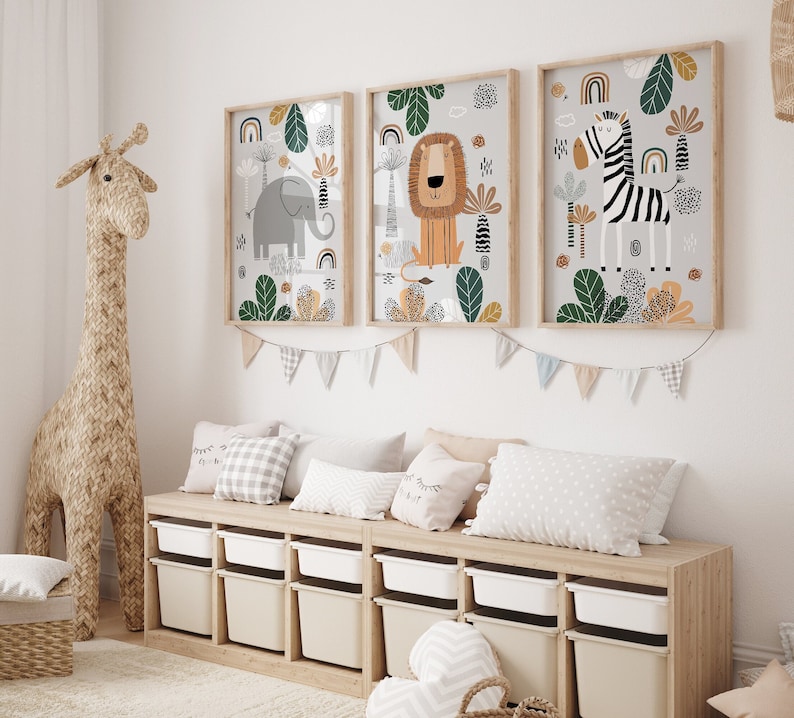 May include: Three framed illustrations of animals in a jungle setting. The illustrations feature a lion, an elephant, and a zebra. The frames are light wood and the illustrations are on a white background.