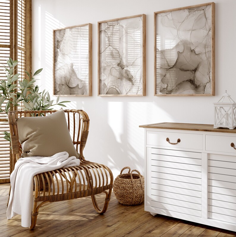 Puede incluir: Un armario blanco con dos cajones y dos puertas, una silla de mimbre con un coj&iacute;n marr&oacute;n y tres impresiones de arte abstracto enmarcadas con dise&ntilde;os de tinta marr&oacute;n y blanco en una pared blanca.