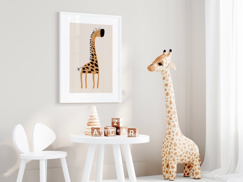 May include: A white framed print of a cartoon giraffe with brown and black spots on a light brown background. A stuffed giraffe toy with brown and white spots stands on a white floor. A white table with a wooden stacking toy and wooden alphabet blocks sits in front of the print. A white chair with bunny ears sits next to the table.