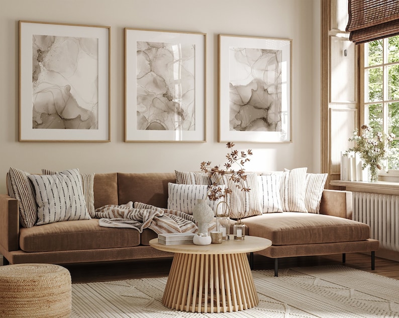 Puede incluir: Un sof&aacute; seccional marr&oacute;n con una manta de tiro marr&oacute;n claro y varias almohadas estampadas. El sof&aacute; est&aacute; en una sala de estar con una mesa de caf&eacute; de madera y tres impresiones de arte abstracto enmarcadas en la pared.