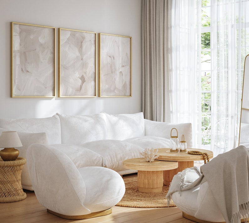 May include: A white sectional sofa with two white accent chairs in a living room with a large window, a wooden coffee table, and three gold candle holders.