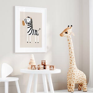 May include: A white framed print of a black and white zebra with a brown background. A white table with a wooden stacking toy and wooden alphabet blocks. A large stuffed giraffe with brown spots stands next to the table. A white chair with bunny ears is in the foreground.