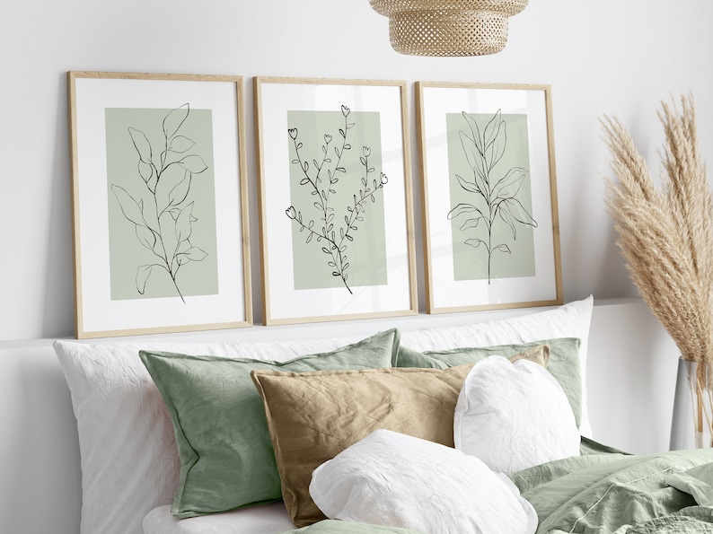 K&ouml;nnte beinhalten: Drei gerahmte Drucke mit minimalistischen Linienzeichnungen von Blatt&auml;sten auf einem Salbeigr&uuml;n-Hintergrund. Die Drucke sind in einer Reihe an einer wei&szlig;en Wand &uuml;ber einem Bett mit gr&uuml;nen und wei&szlig;en Kissen angeordnet.