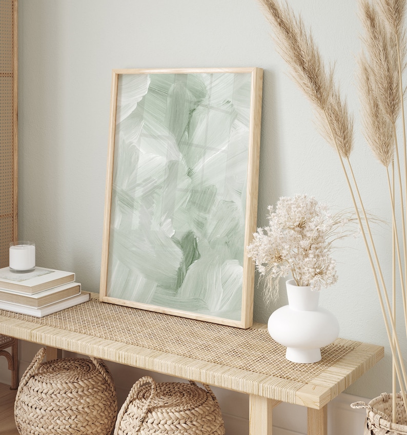 May include: A wooden bench with a woven rattan top, two woven baskets, and a vase with dried flowers. A framed abstract painting with green brushstrokes hangs above the bench.