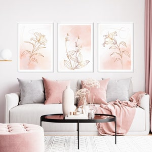 May include: Three framed prints with a minimalist design featuring gold line drawings of flowers and leaves on a pink watercolor background.