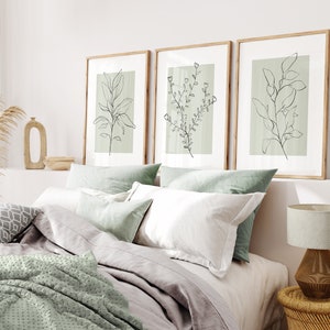 K&ouml;nnte beinhalten: Drei gerahmte Drucke mit minimalistischen Linienzeichnungen von Pflanzen auf hellgr&uuml;nem Hintergrund. Die Drucke h&auml;ngen an einer wei&szlig;en Wand &uuml;ber einem Bett mit wei&szlig;er und gr&uuml;ner Bettw&auml;sche.