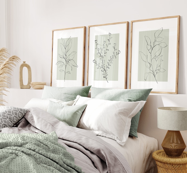 K&ouml;nnte beinhalten: Drei gerahmte Drucke mit minimalistischen Linienzeichnungen von Pflanzen auf hellgr&uuml;nem Hintergrund. Die Drucke h&auml;ngen an einer wei&szlig;en Wand &uuml;ber einem Bett mit wei&szlig;er und gr&uuml;ner Bettw&auml;sche.