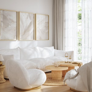 May include: A white living room with a white sofa, two white chairs, a wooden coffee table, and three framed abstract paintings on the wall. The room has a large window with white curtains and a mirror on the wall.