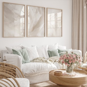 May include: A white sofa with light green cushions and a white throw. A vase of pink flowers sits on a wooden coffee table in front of the sofa. Three framed abstract art prints hang on the wall behind the sofa.