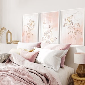 May include: Three framed prints with a pink watercolor background and gold line drawings of flowers. The prints are hanging on a white wall above a bed with pink bedding.