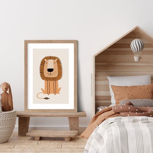 May include: A framed print of a cartoon lion with a brown mane and a light brown body. The lion is sitting with its paws crossed and has a friendly expression. The print is on a white background and is framed in a light brown wood frame.