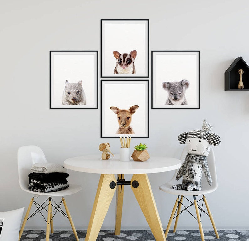 May include: Five framed animal prints on a white wall, featuring a koala, a wombat, a sugar glider, a kangaroo, and a joey. The prints are arranged in a grid pattern, with the sugar glider print in the top center. The prints are all black and white, except for the kangaroo print, which is in color. The prints are all in a modern style, with simple frames and clean lines.