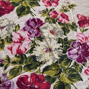 K&ouml;nnte beinhalten: Eine Tischdecke mit floralem Muster mit einem sich wiederholenden Muster aus gro&szlig;en, farbenfrohen Blumen. Die Blumen sind in Rot-, Rosa-, Lila- und Wei&szlig;t&ouml;nen gehalten, mit gr&uuml;nen Bl&auml;ttern. Der Hintergrund ist cremefarben mit einem dezenten Rautenmuster.