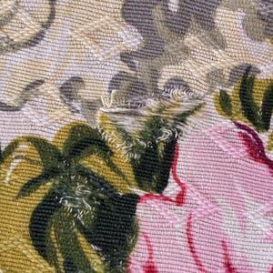 K&ouml;nnte beinhalten: Nahaufnahme eines Stoffes mit floralem Muster. Das Design zeigt gro&szlig;e rosa und rote Blumen mit gr&uuml;nen Bl&auml;ttern vor einem beige-grauen Hintergrund. Der Stoff hat ein strukturiertes Aussehen mit sichtbaren N&auml;hten.