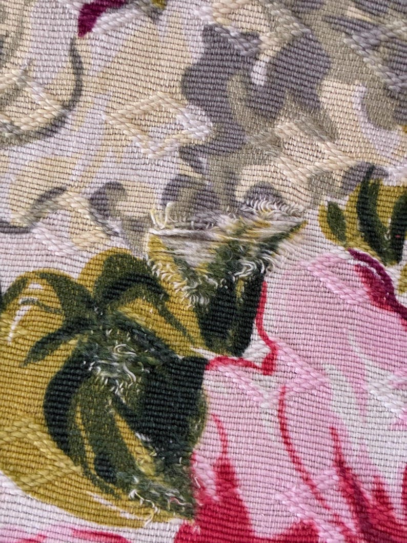 K&ouml;nnte beinhalten: Nahaufnahme eines Stoffes mit floralem Muster. Das Design zeigt gro&szlig;e rosa und rote Blumen mit gr&uuml;nen Bl&auml;ttern vor einem beige-grauen Hintergrund. Der Stoff hat ein strukturiertes Aussehen mit sichtbaren N&auml;hten.