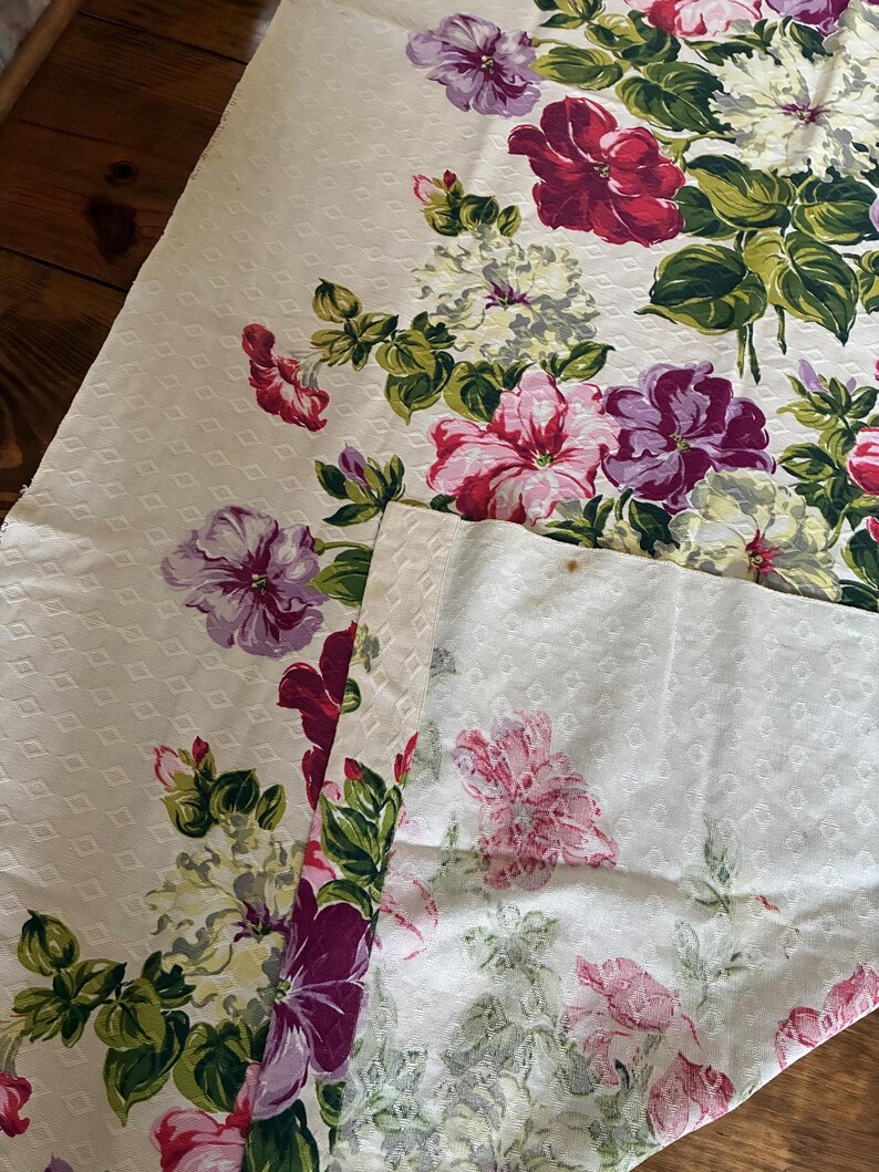 K&ouml;nnte beinhalten: Cremefarbener Stoff mit floralem Muster und sich wiederholendem Rautenmuster. Der Stoff ist mit gro&szlig;en, leuchtenden Blumen in Rot-, Rosa-, Lila- und Wei&szlig;t&ouml;nen mit gr&uuml;nem Laub verziert. Der Stoff wird wahrscheinlich f&uuml;r Heimdekoration oder Bastelarbeiten verwendet.