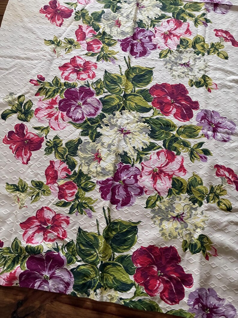 K&ouml;nnte beinhalten: Cremefarbener Blumenstoff mit einem sich wiederholenden Rautenmuster. Er zeigt gro&szlig;e Bl&uuml;ten in Rot, Rosa, Lila und Wei&szlig; mit gr&uuml;nen Bl&auml;ttern. Das Design ist ein klassisches Blumenmuster, geeignet f&uuml;r verschiedene Textilanwendungen.
