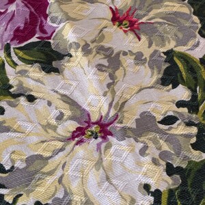 K&ouml;nnte beinhalten: Nahaufnahme eines floralen Stoffes mit gro&szlig;en, strukturierten Blumen in Creme-, Grau- und Gelbt&ouml;nen. Die Blumen haben rote und violette Zentren, umgeben von gr&uuml;nen Bl&auml;ttern. Der Stoff hat ein gewebtes Aussehen.