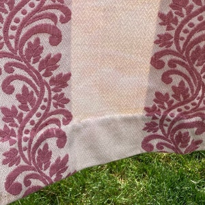 May include: A cream-colored fabric featuring a woven herringbone texture and vertical bands of raised, dark pink floral embroidery. The textile displays a repeating pattern of scrolling leaves and vines that run parallel across the surface.