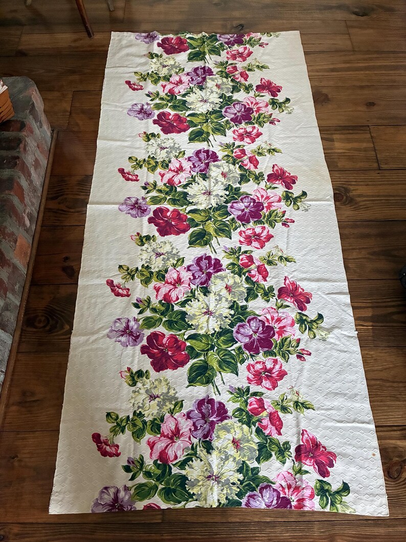 K&ouml;nnte beinhalten: Cremefarbener Stoff mit einem Blumenmuster aus roten, rosa, lila und wei&szlig;en Bl&uuml;ten. Gr&uuml;ne Bl&auml;tter und Stiele sind mit den Bl&uuml;ten verwoben. Der rechteckige Stoff liegt auf einer Holzoberfl&auml;che.