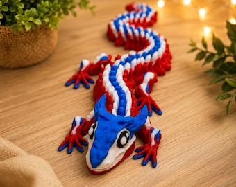 Puede incluir: Una figura de lagarto articulada impresa en 3D con un esquema de colores vibrantes en rojo, blanco y azul. La criatura tiene un diseño de cuerpo texturizado y segmentado con una cabeza azul, grandes ojos negros y blancos, y cuatro extremidades.