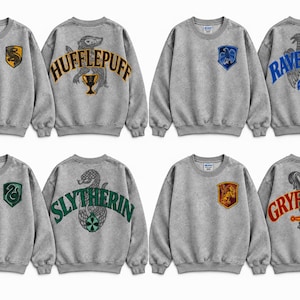 May include: A collection of four grey crewneck sweatshirts, each featuring a small house crest on the front left chest and a large house name with a corresponding animal emblem and symbol printed on the back in vibrant colors.