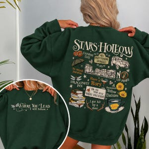 May include: A dark green crewneck sweatshirt featuring a large back graphic with the text Stars Hollow and various illustrations including a car, books, and a coffee cup. The front chest area displays the text Where You Lead I will follow.