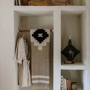 May include: A neutral-toned, built-in shelving unit with decorative items. A beige robe hangs on a wooden rod, next to a patterned blanket. Shelves hold books, a candle holder, a vase, and other decor.