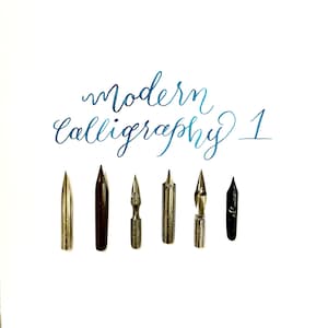 Pode incluir: Sete diferentes pontas de caligrafia, incluindo uma ponta preta, uma ponta prateada e uma ponta dourada. As pontas est&atilde;o dispostas em uma fileira sobre um fundo branco. O texto "modern calligraphy 1" est&aacute; escrito em tinta azul acima das pontas.