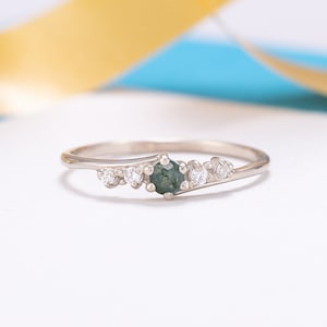May include: A delicate silver ring with a green gemstone and small white gemstones set in a curved band.