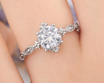 May include: A silver-toned ring featuring a large, round, clear faceted center stone held by multiple prongs. The band is crafted with intricate metalwork, including small bead-like details and a delicate, textured pattern along the shank.