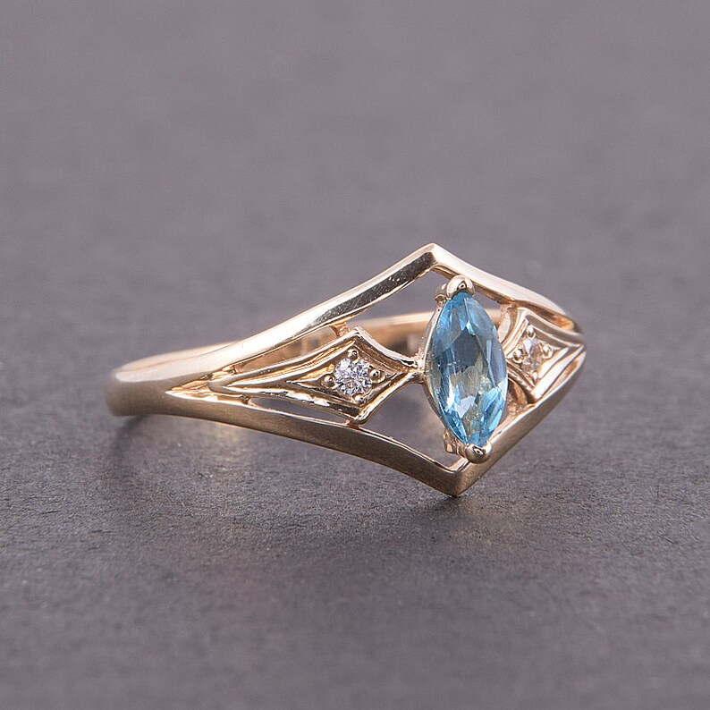 May include: A gold ring with a marquise-shaped blue topaz gemstone and two smaller round diamonds. The ring has a delicate, intricate design.