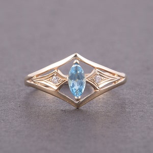 May include: A gold ring with a marquise-shaped blue topaz gemstone and two smaller round diamonds set in a delicate, geometric design.