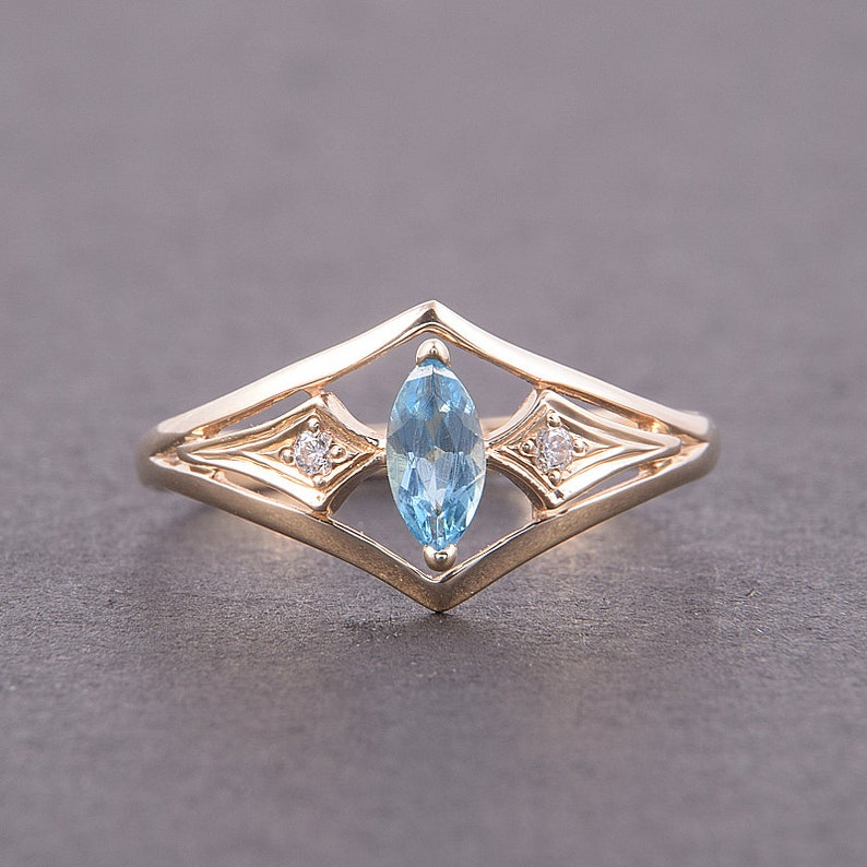 May include: A gold ring with a marquise-shaped blue topaz gemstone and two smaller round diamonds set in a delicate, geometric design.
