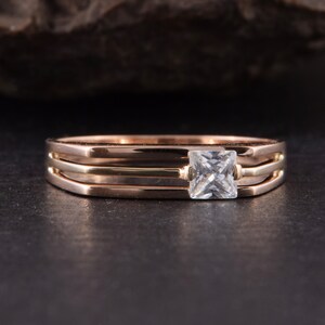 May include: A gold ring with three bands and a square-shaped clear gemstone in the center.