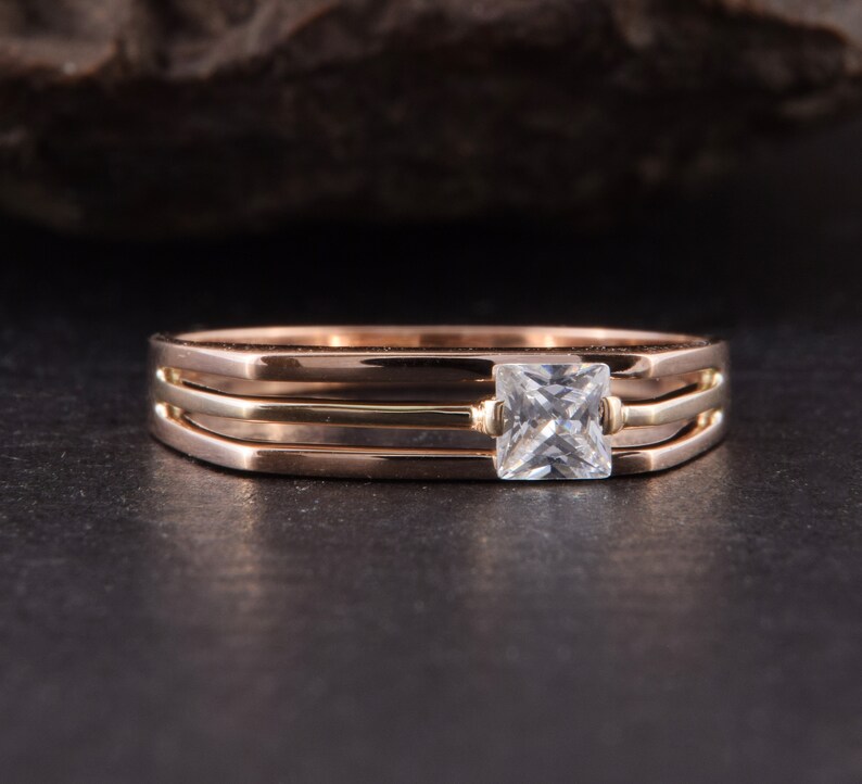 May include: A gold ring with three bands and a square-shaped clear gemstone in the center.