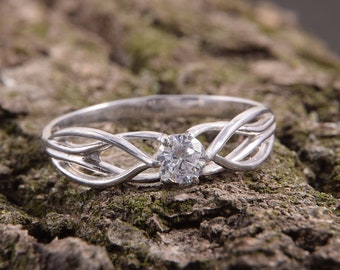 Könnte beinhalten: Ein silberner Ring mit einem filigranen, verflochtenen Design, das mit einem einzigen, runden, klaren Edelstein verziert ist.