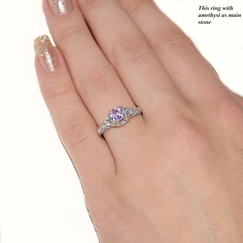 May include: A silver-toned ring featuring a round, light purple amethyst as the main stone, surrounded by small clear accent stones along the band. The text "This ring with amethyst as main stone" is visible in the upper right corner of the image.