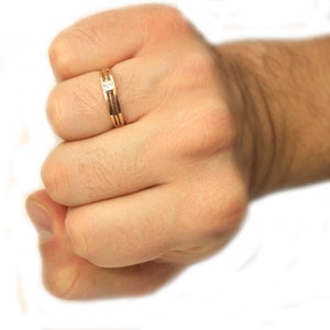 May include: A gold band ring with a single, clear, square-shaped gemstone.