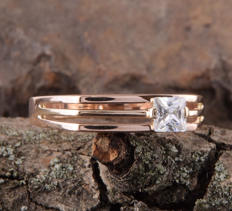 May include: A rose gold ring with three bands and a square-shaped clear gemstone.