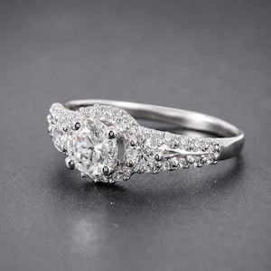 May include: A silver-toned ring featuring a large round-cut center stone surrounded by a halo of smaller pav&eacute;-set stones. The band is split and adorned with additional small round stones along the shoulders and sides of the central setting.