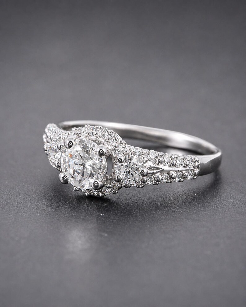 May include: A silver-toned ring featuring a large round-cut center stone surrounded by a halo of smaller pav&eacute;-set stones. The band is split and adorned with additional small round stones along the shoulders and sides of the central setting.