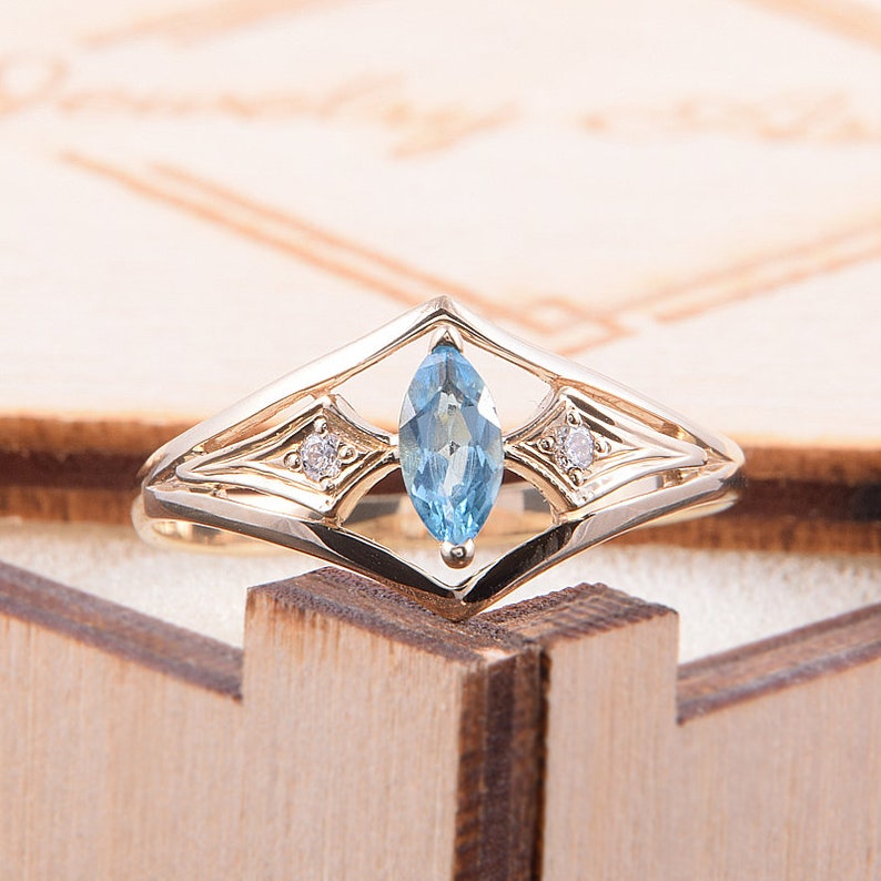 May include: A gold ring with a marquise-shaped blue topaz gemstone and two smaller round diamonds. The ring has a delicate, intricate design.